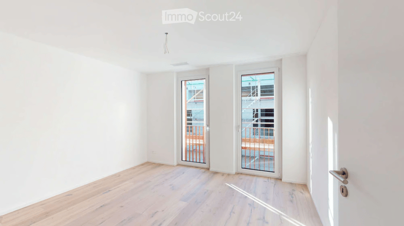 Empty room with white walls, light wooden flooring, and two glass doors leading to a balcony area.