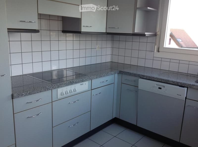 Modern kitchen with white cabinets, granite countertops, a built-in stove, and a dishwasher. The walls are tiled, and there is a window providing natural light.