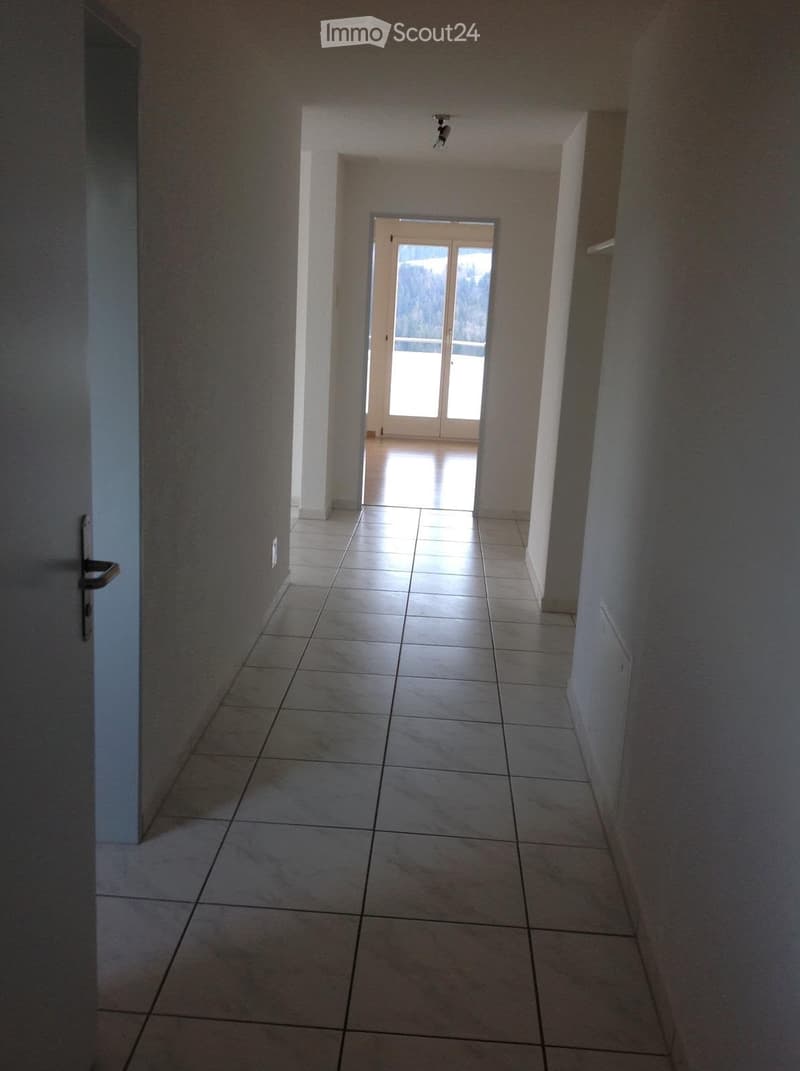 Empty hallway with tiled floor, white walls, and a sliding glass door at the end leading to a view.