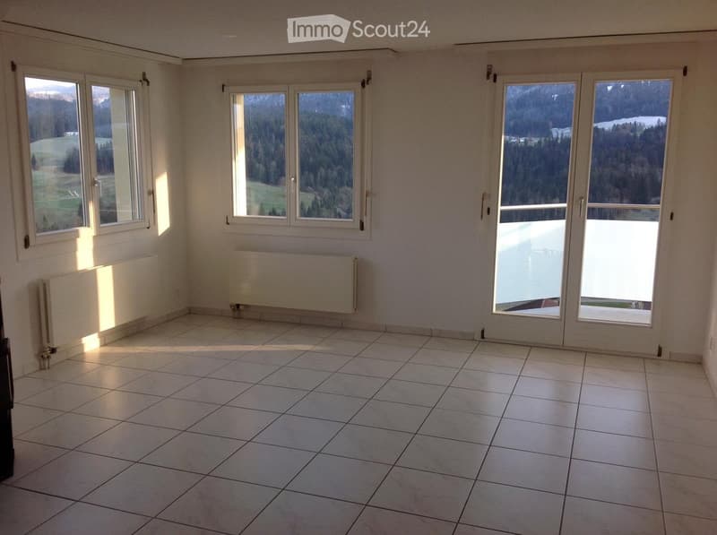 Empty room with tiled floor, large windows, radiators, and a sliding glass door leading to a balcony.
