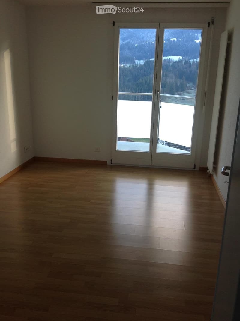 Empty room with wooden flooring and large sliding glass doors leading to a balcony with a scenic mountain view.