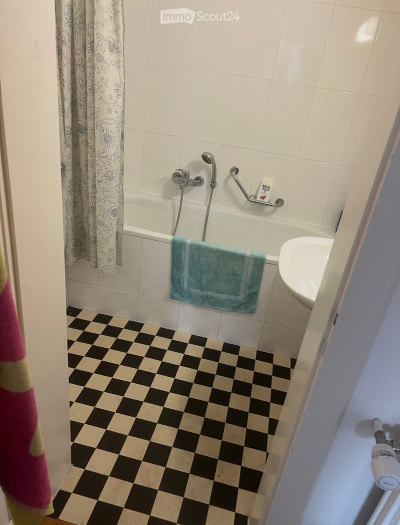 Bathroom with a bathtub, showerhead, towel, and sink. The floor has a black and beige checkered pattern.