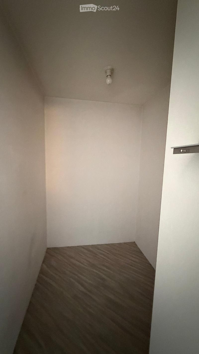 Empty room with light-colored walls and a wooden floor, featuring a single light fixture on the wall.