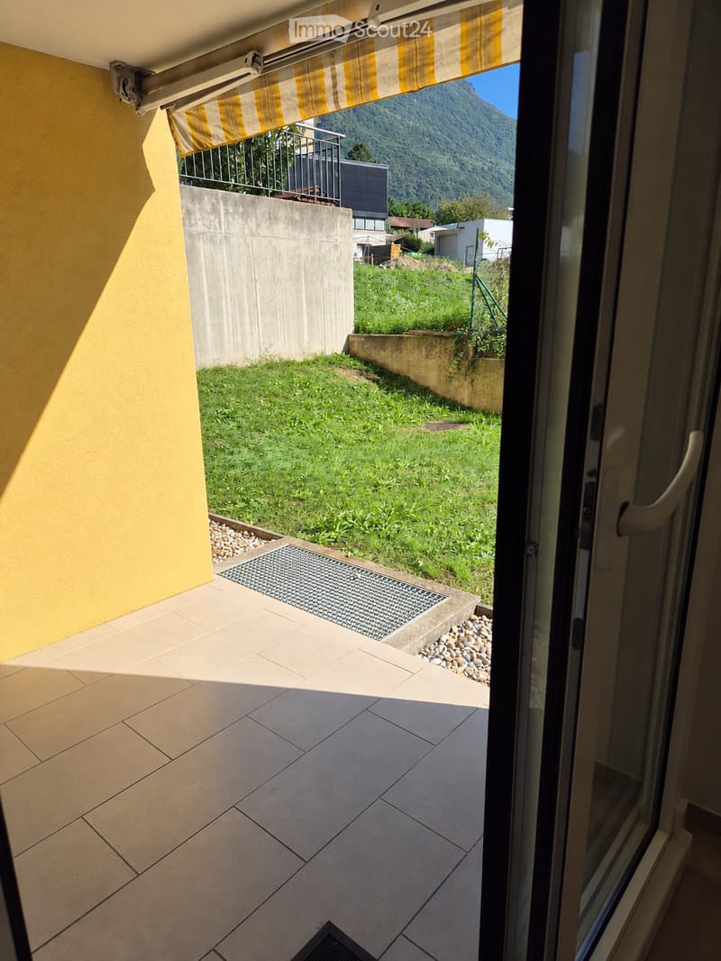 Balcony with tiled floor, yellow wall, view of green lawn and mountains, covered by striped awning.