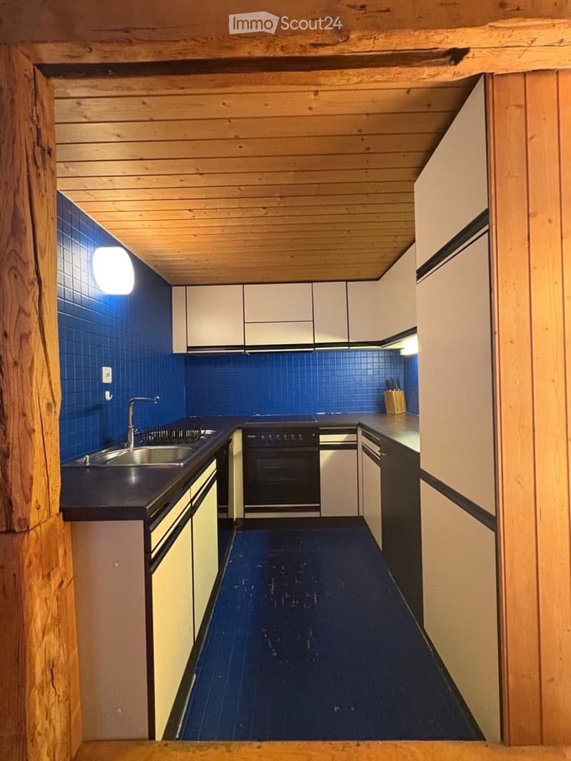 Modern kitchen with white cabinets, blue tiled backsplash, dark countertops, and a stainless steel sink and oven.