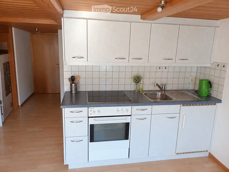 Modern kitchen with white cabinets, grey countertops, and a stainless steel sink. Features an induction stove, oven, and various kitchen utensils.