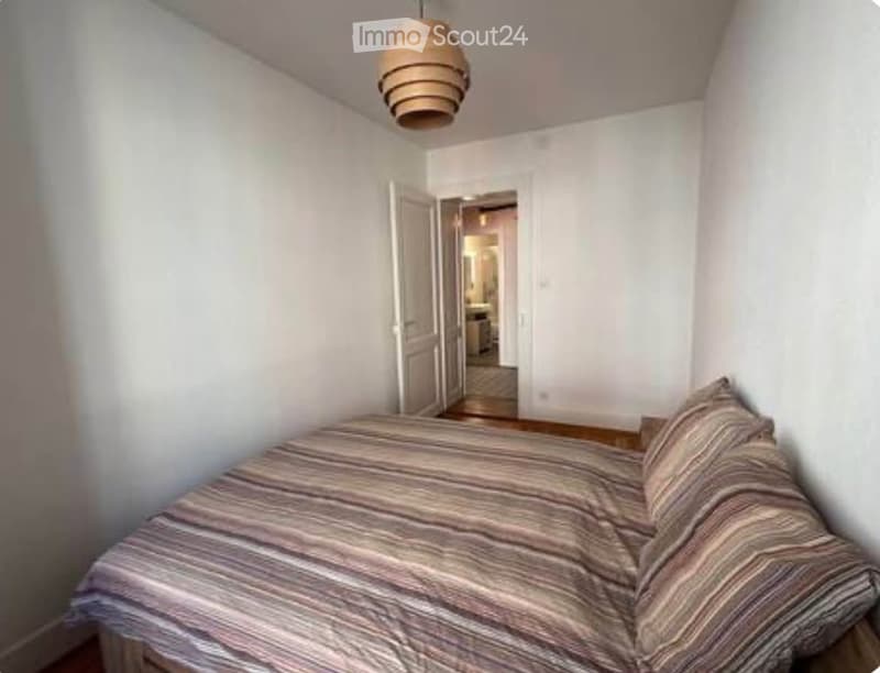 Cozy bedroom with a neatly made bed, striped bedding, and a pendant light hanging from the ceiling. An open door leads to another room.