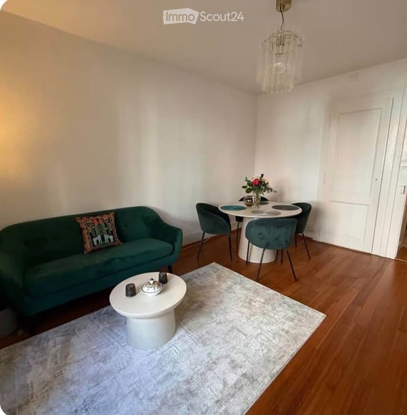 A modern living and dining area with a green sofa, white coffee table, dining table with chairs, and a chandelier.