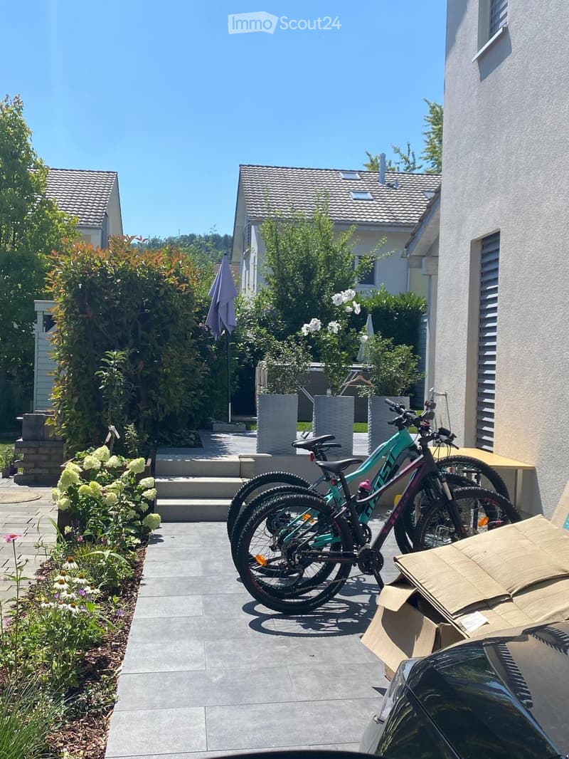 Garden area with paved pathway, bicycles, plants, and a small staircase leading to a house entrance.