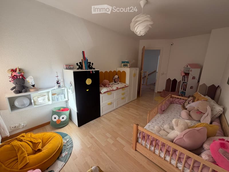 A well-lit children's bedroom with a wooden bed, colorful pillows, a wardrobe, shelves with toys, and a yellow bean bag chair.