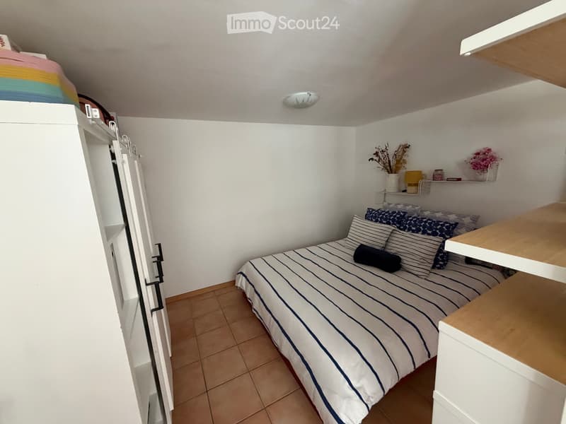 Cozy bedroom with a single bed, nightstand, shelves, and decorative items.