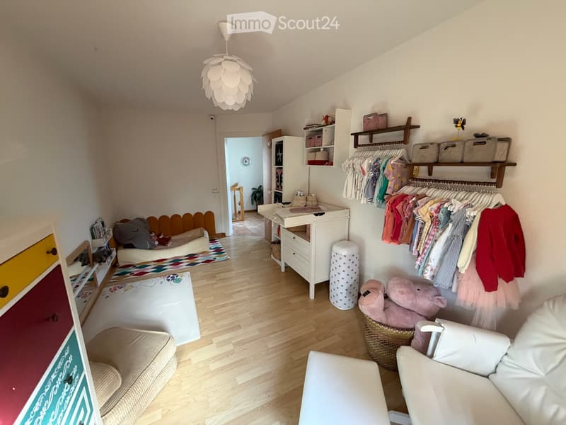 A well-organized children's room with a wooden floor, a white lamp, a small sofa, a chair, a changing table, shelves, and storage bins.