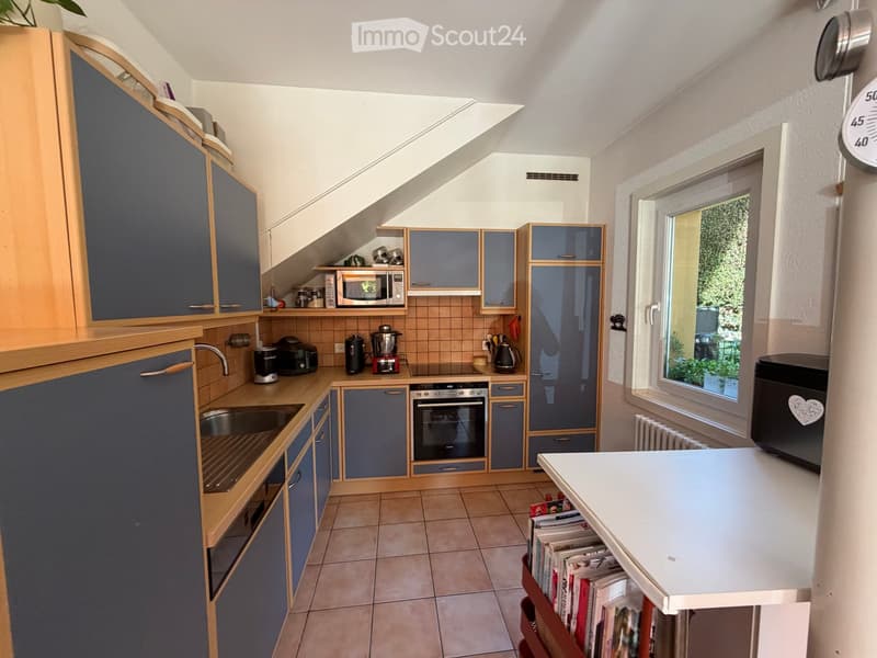 Modern kitchen with blue and wood cabinets, stainless steel appliances, and a large window offering a view of greenery.