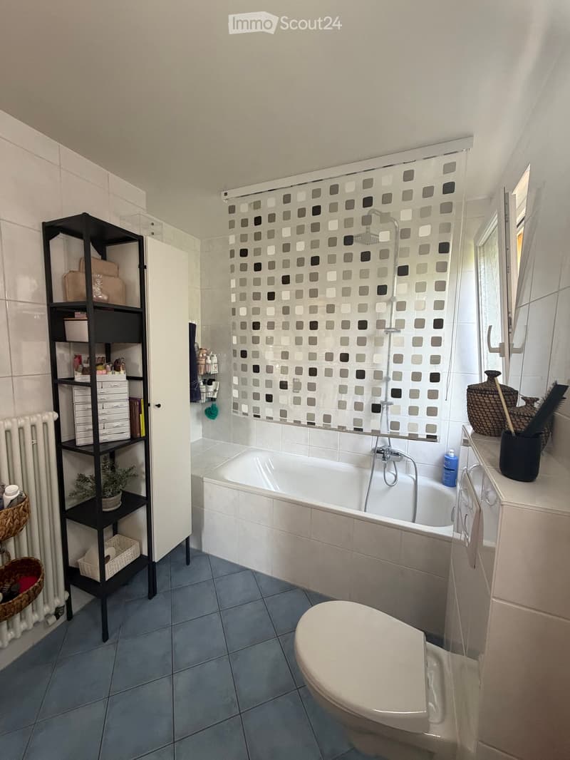 Modern bathroom with a bathtub, toilet, shower curtain, shelf, radiator, mirror, and decorative baskets.