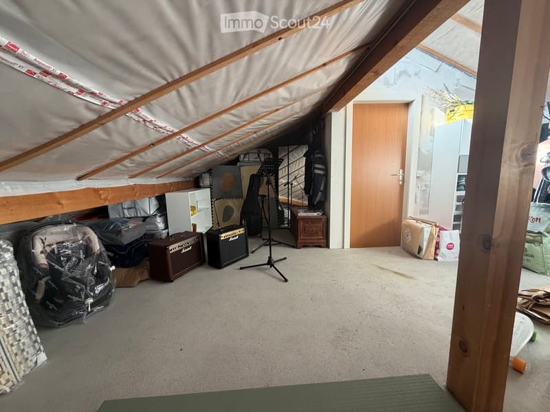 An attic space with wooden beams and slanted ceilings, featuring musical equipment including guitars, amplifiers, and a guitar stand, along with storage items and a small cabinet.