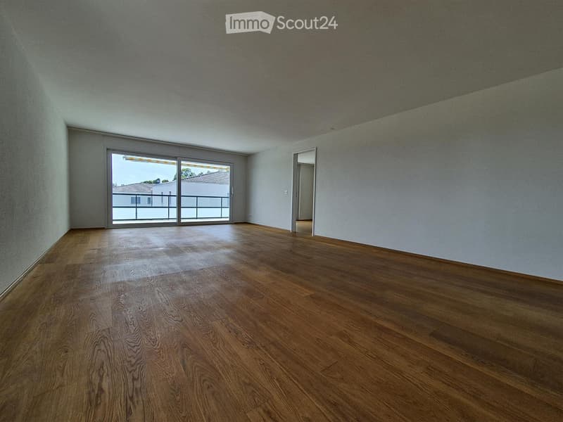 Empty room with wooden flooring, white walls, and large sliding glass doors leading to a balcony.