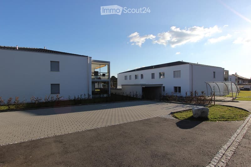 Modern two-story building with white exterior, garage, and small landscaped area with a stone and grass patch.