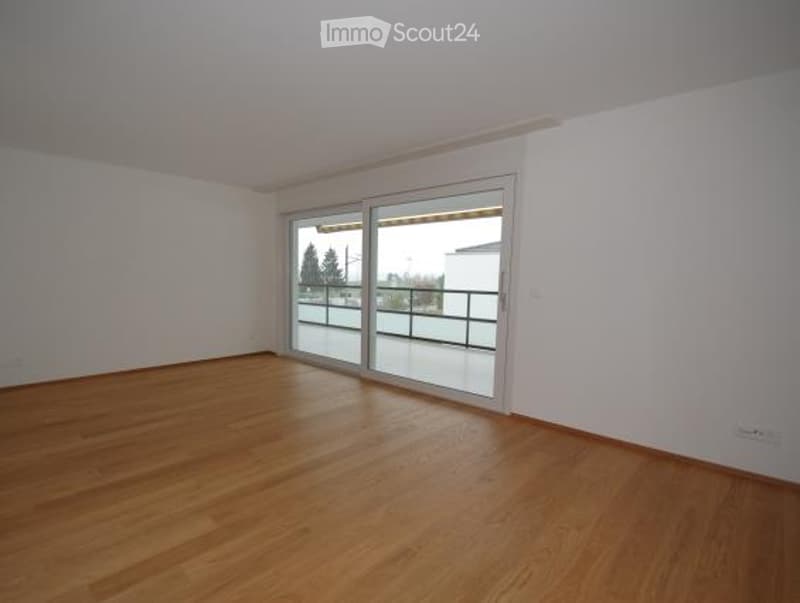 Empty room with wooden flooring, white walls, and large sliding glass doors leading to a balcony.