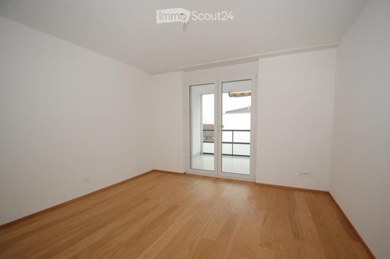 Empty room with wooden flooring, white walls, and a sliding glass door leading to a balcony.