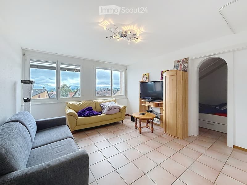 Bright living room with large windows, two sofas, a coffee table, a TV on a stand, and a wooden wardrobe.