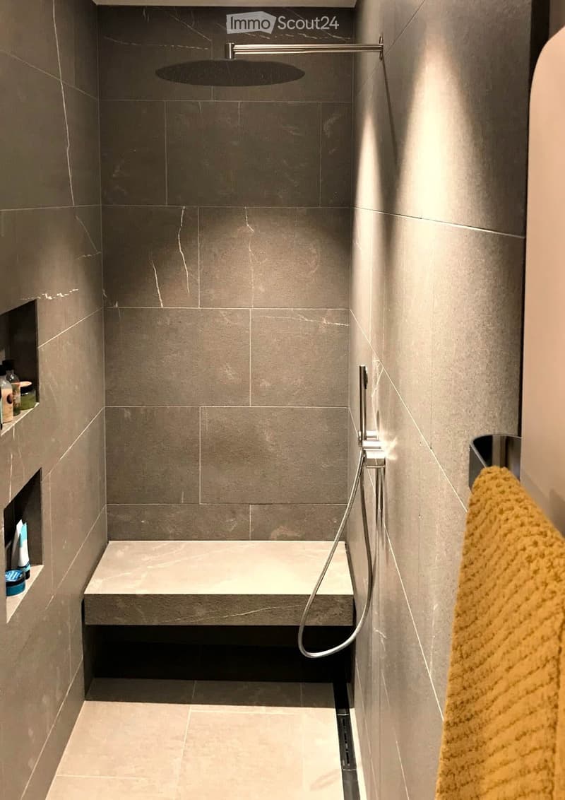 Modern shower area with grey marble tiles, a built-in seat, and a handheld showerhead.