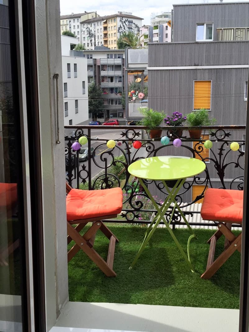 Balcony with green table, orange chairs, small potted plants, and decorative string lights.
