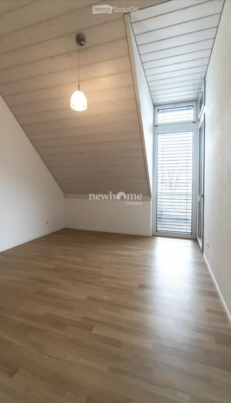 Empty room with wooden flooring, white walls, and a hanging light fixture. Features a large window with blinds and a door leading outside.