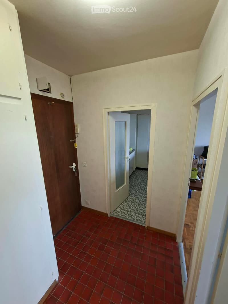 A narrow hallway with red tiled flooring, white walls, and several doors leading to different rooms.