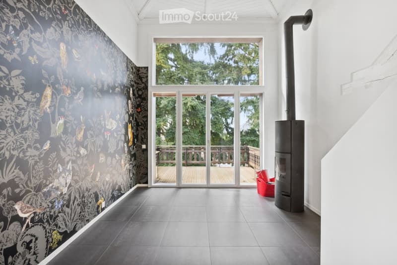 Modern, minimalist room with dark grey tiled floor, large windows, and a decorative mural featuring birds and foliage. A wood stove and a red chair are visible.