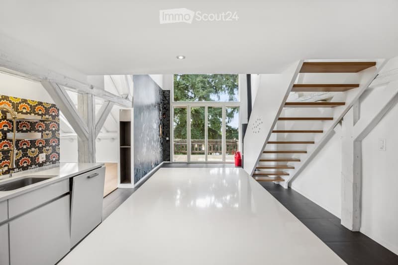Modern kitchen with white cabinets, a sleek sink, and a staircase leading upwards. The space features a colorful backsplash and large windows offering a view of the outdoor area.