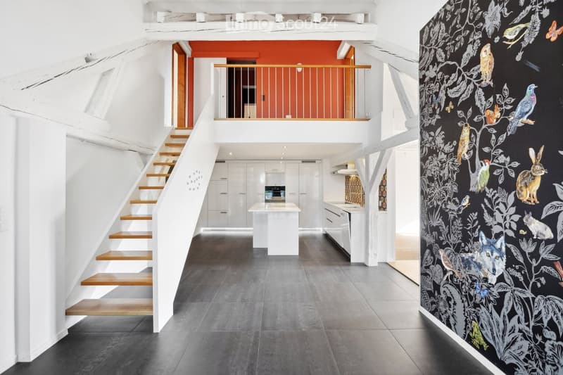 Open-plan hallway with a staircase leading to an upper level, modern kitchen area with white cabinets and a central island, and a decorative black wall mural featuring animals and foliage.