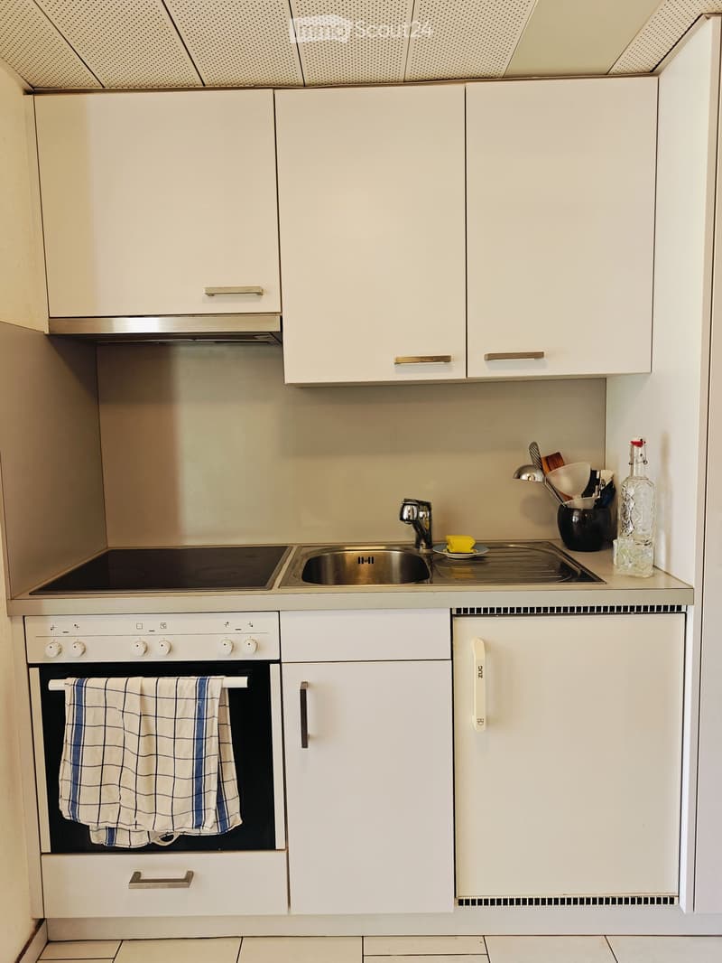 Modern kitchen with white cabinets, stainless steel sink, oven, and various kitchen items on the counter.