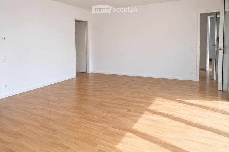 Empty room with light wooden flooring and white walls, featuring two doors and electrical outlets.