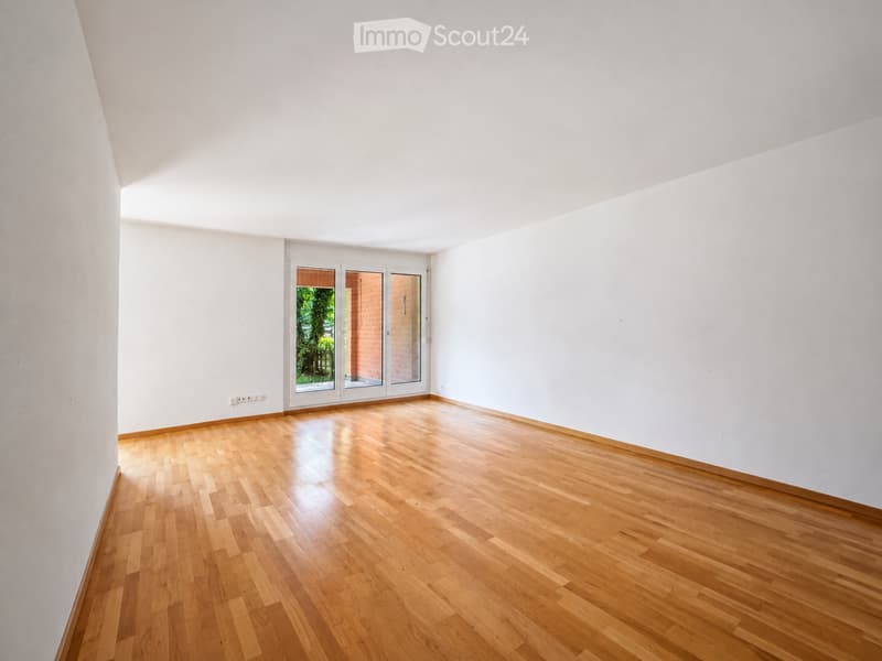 Empty room with light wooden flooring, white walls, and large glass doors leading to an outdoor area.