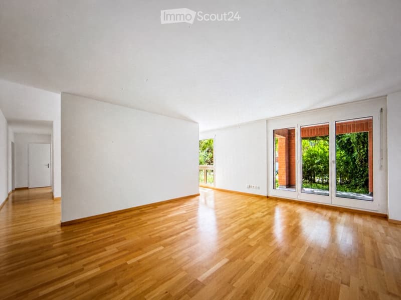 Empty room with light wooden flooring, white walls, and large windows with sliding glass doors leading to a balcony.
