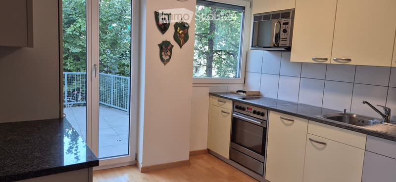 Modern kitchen with white cabinets, stainless steel oven, microwave, and sink. Features a balcony with a view of greenery.