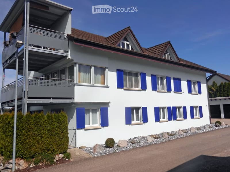white house, brown roof, blue shutters, balcony, gravel driveway