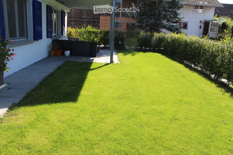 well-maintained lawn, hedges, outdoor seating area with a sofa, potted plants, and a pathway