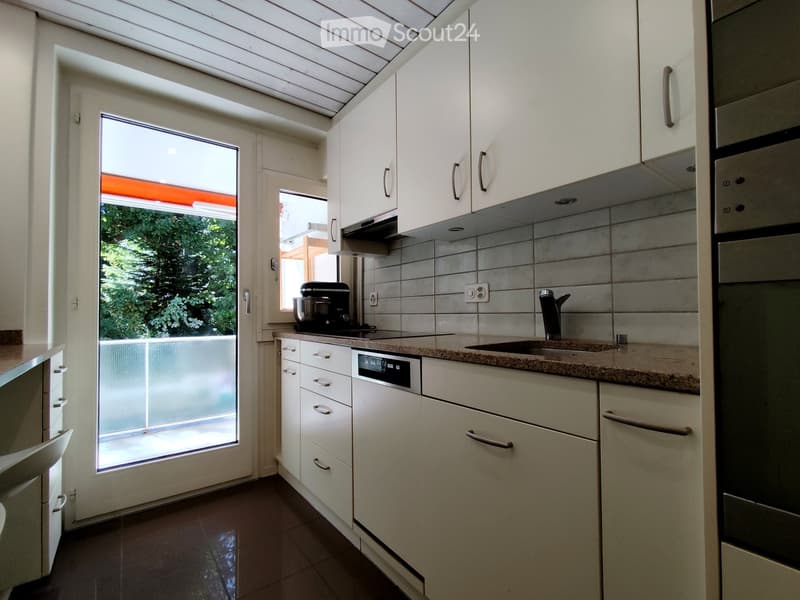 Modern kitchen with white cabinets, granite countertops, stainless steel appliances, and a large window overlooking a green area.