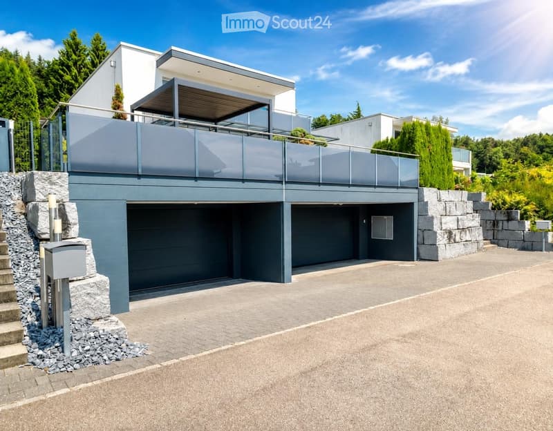 Modern two-story house with a grey garage, a raised balcony, and a stone staircase leading to the entrance.