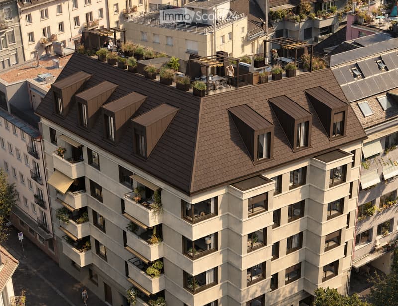 A modern multi-story residential building with balconies, rooftop terraces, and greenery. The building features a brown tiled roof and large windows.