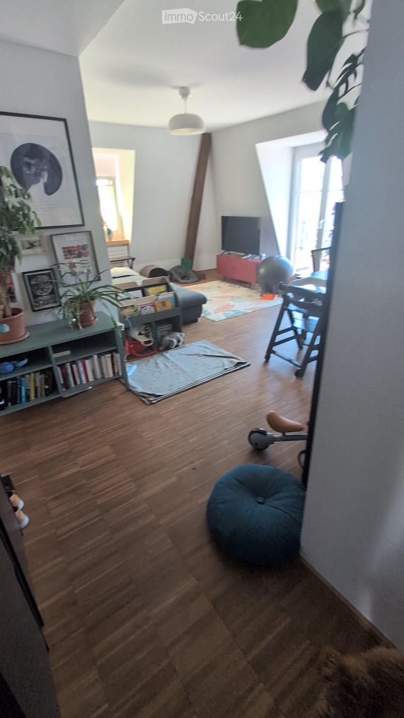 Living room with wooden flooring, a sofa, bookshelf, a ball, a chair, a table, a lamp, picture frames, and a stool.