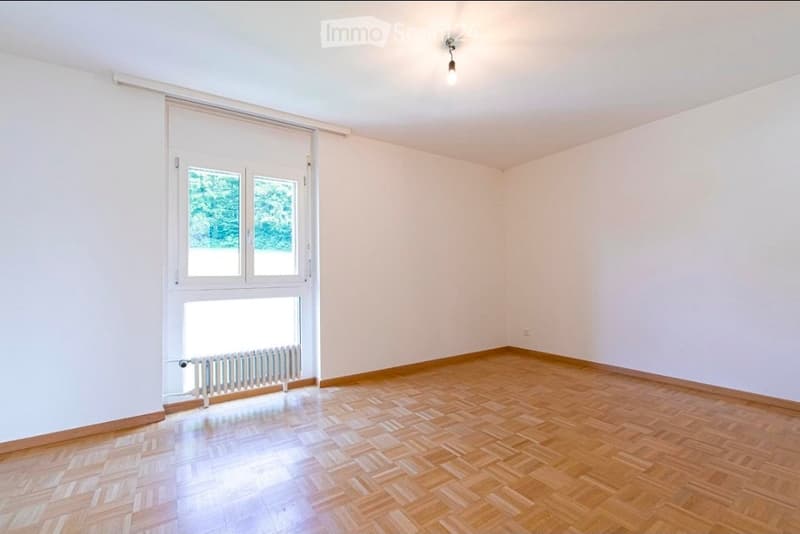 Empty room with wooden flooring, white walls, large windows, and a radiator under the window.