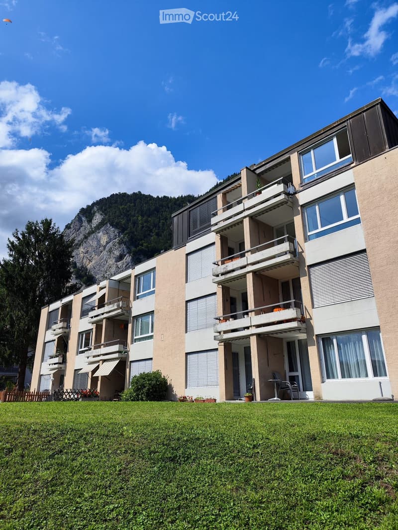 Multi-story residential building with balconies, large windows, and a well-maintained lawn in front.