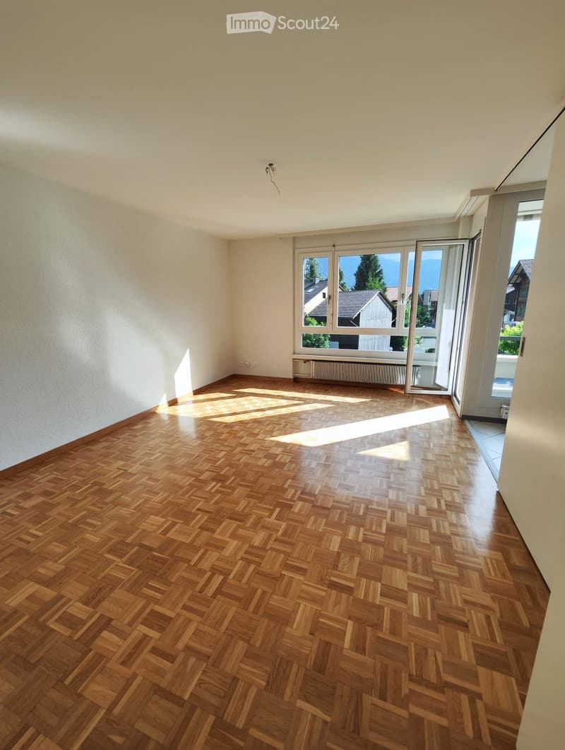Empty room with wooden herringbone flooring, white walls, and large windows with a view of the outside. No furniture or equipment is present.