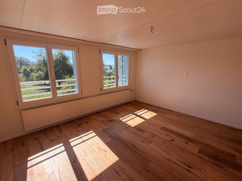 Empty room with wooden flooring, large windows, and radiators. Natural light streams in, casting shadows on the floor.