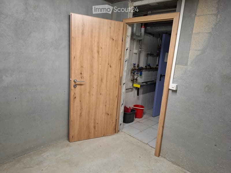 An unfurnished utility room with a wooden door, exposed pipes, and a small sink area with buckets.