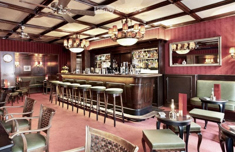 Elegant bar area with wooden bar counter, multiple bar stools, plush seating, small tables, and decorative lighting.