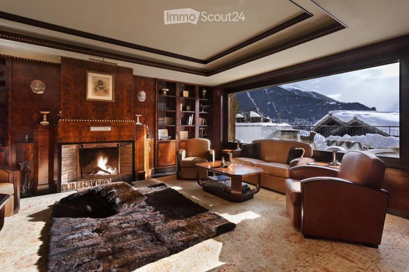 Elegant living room with a fireplace, leather sofa, armchairs, coffee table, bookshelf, and a scenic mountain view through large windows.