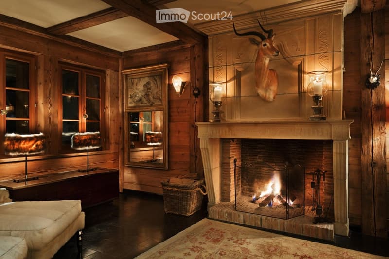 Cozy living room with wooden walls, a lit fireplace, a large animal head mounted on the wall, and warm lighting from table lamps and wall-mounted lamps.